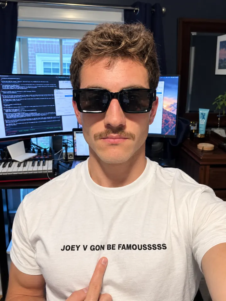 Joey Viola at his desk, in a shirt that reads JOEY V GON BE FAMOUSSSSS